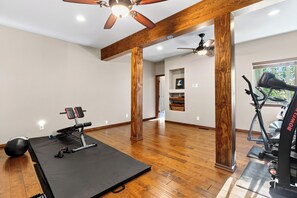 Ein geräumiges Zimmer mit Deckenventilator, Holzbalken, Laufband und Langhantelbank.