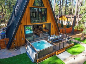 Ein modernes Chalet im A-Rahmen-Stil mit Whirlpool, Sitzgelegenheit im Freien und einer Terrasse mit Blick auf einen bewaldeten Bereich.