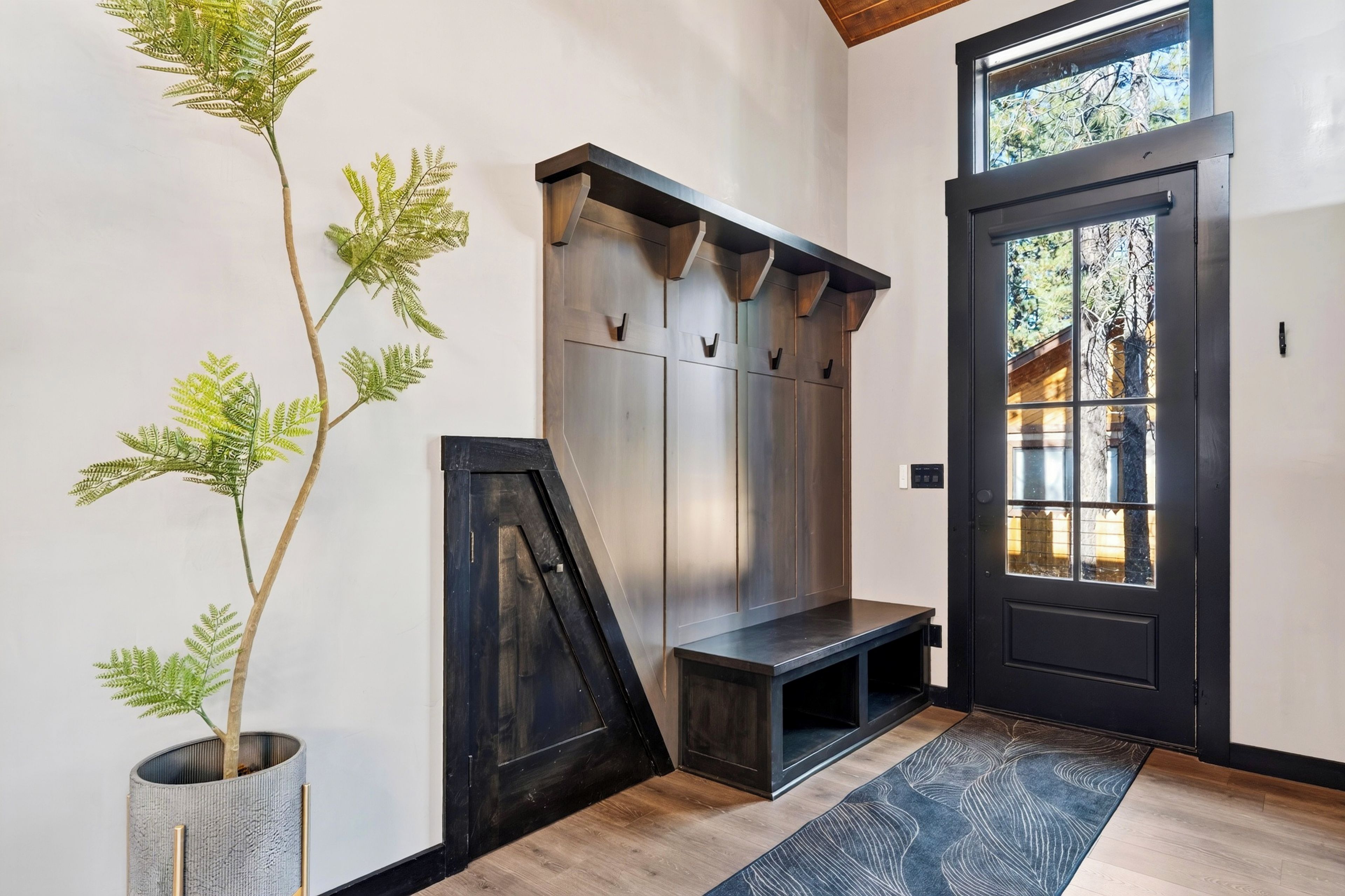 Un hall d’entrée moderne avec un banc, des patères et une plante en pot.