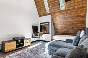 Ein modernes Schlafzimmer mit schrägen Wänden, integriertem Fernseher, einer bequemen Couch und einer Wand als Holzdekor.