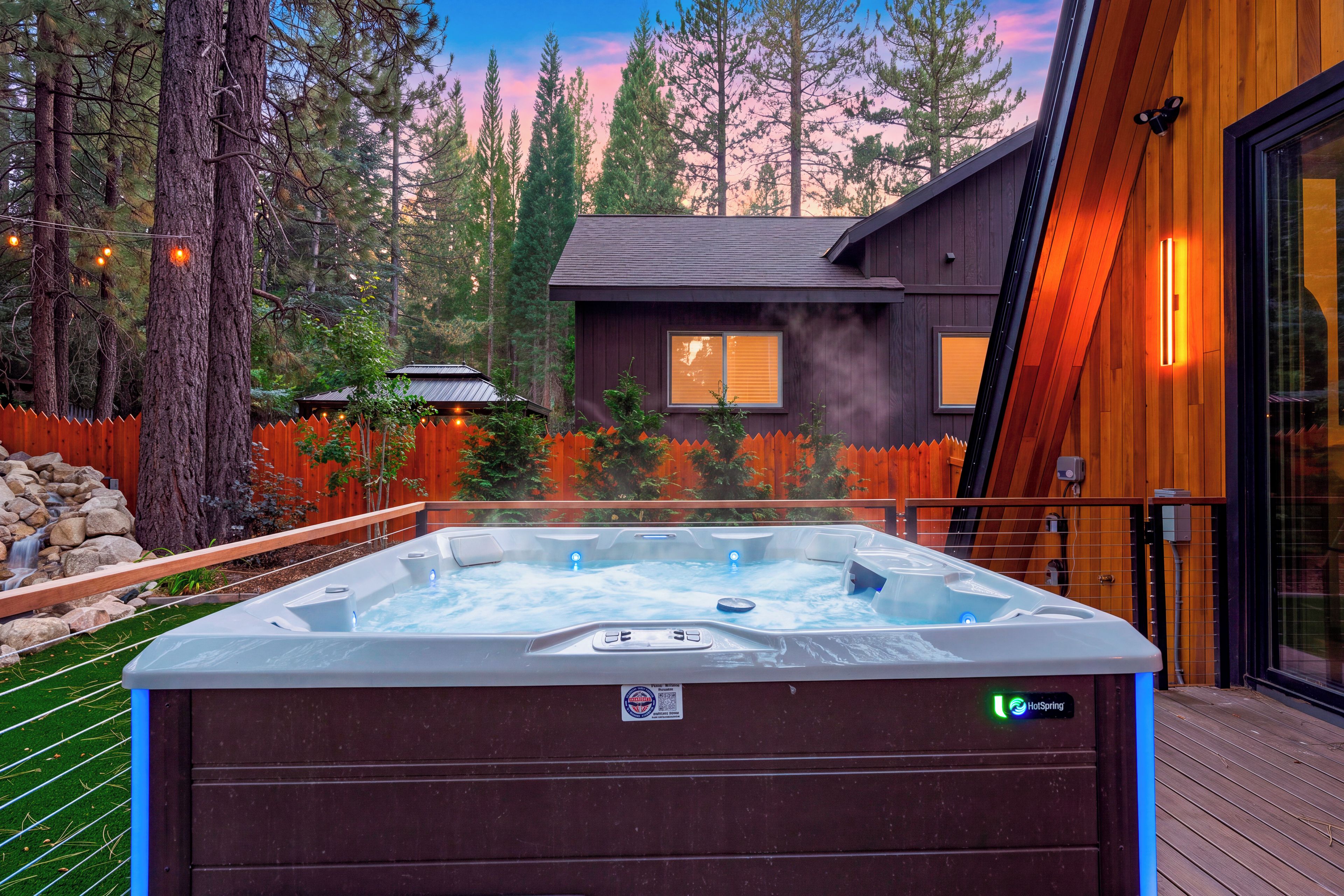 Ein Whirlpool auf einer Holzdielen-Terrasse mit Blick auf eine Holzhütte und Wald.