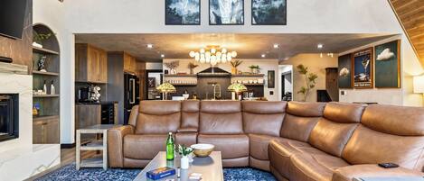 A spacious living room with a large leather sectional sofa, a coffee table, and a fireplace.