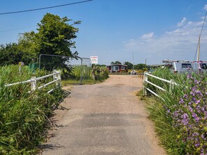 A gravel path leading to a gated area with a no parking sign, surrounded by greenery and a small building. - 2 bedroom accommodation in Repps-with-Bastwick (Repps-with-Bastwick)