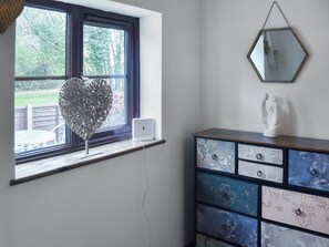 Ein Zimmer mit Fenster, einem weißen Lautsprecher, einer herzförmigen Dekoration, einem Schminktisch mit Blumenmuster und einem sechseckigen Spiegel.