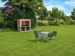 A grassy outdoor area with a brick barbecue grill and a metal table with chairs. - 2 bedroom accommodation in Repps-with-Bastwick (Repps-with-Bastwick)