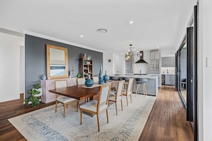 A modern kitchen with a central island, a dining area with a wooden table and chairs, and a large mirror on the wall. - Fletchers Ridge House (Montville)