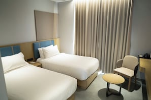 A hotel room with two beds, a chair, a small table, and a curtain.