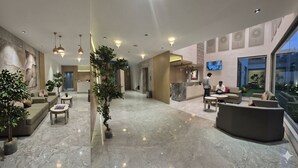 Een moderne hotellobby met een receptiebalie, een zithoek en een groot raam met uitzicht.