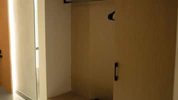 A wooden wardrobe with multiple shelves and a hanging rod, located in a hallway with a glass door on the left.