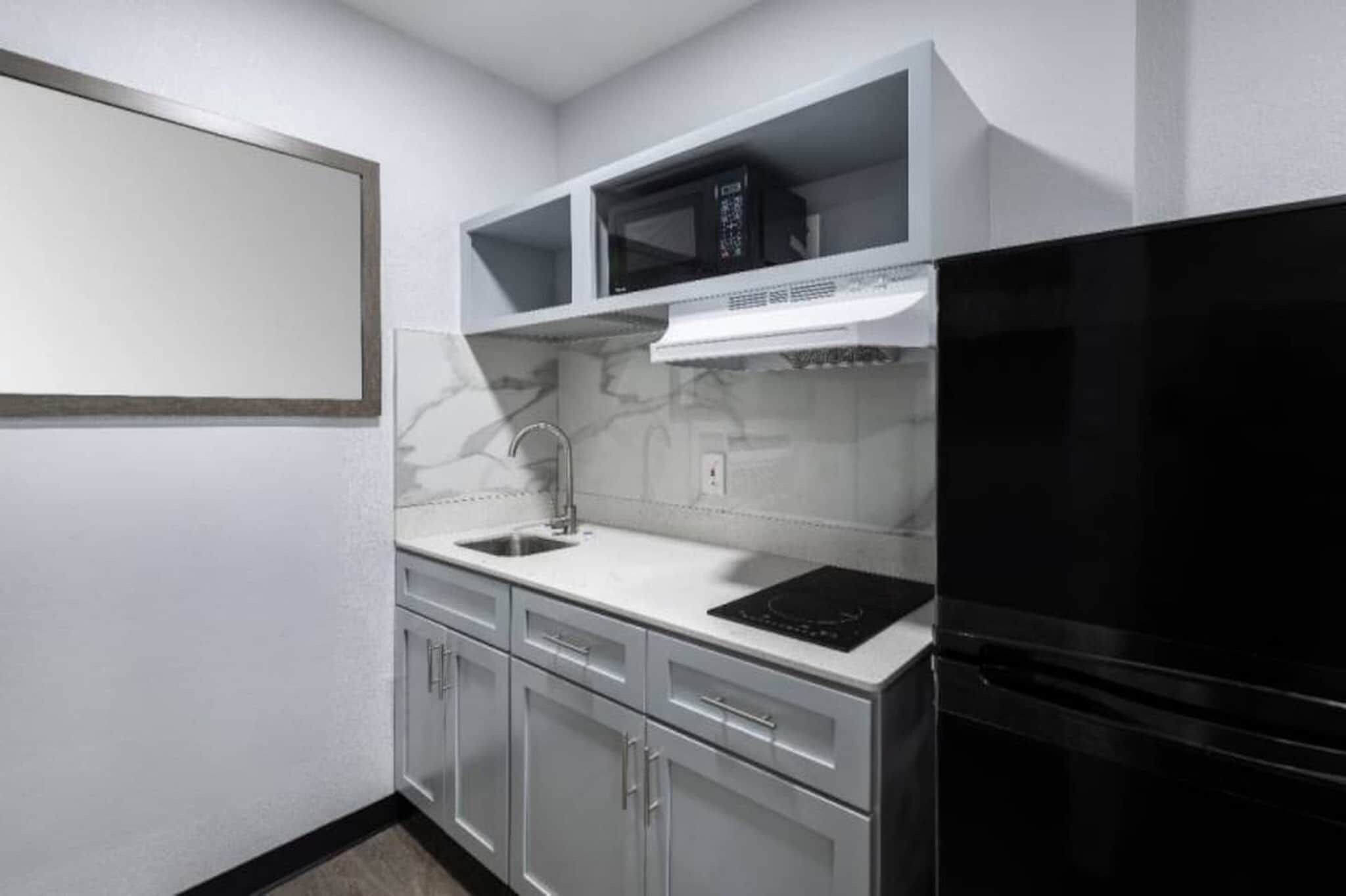 A compact kitchen with a black refrigerator, a microwave, and a stainless steel sink.