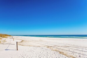 Una platja amb cel clar, sorra daurada i onades oceàniques.