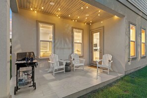 An outdoor patio area with two white Adirondack chairs, a grill cart with bottles, and a tiled floor. - Golf Cart + Arcade Game Room | Pool Access | 5 Min to Beach | Costal 45 (Miramar Beach)
