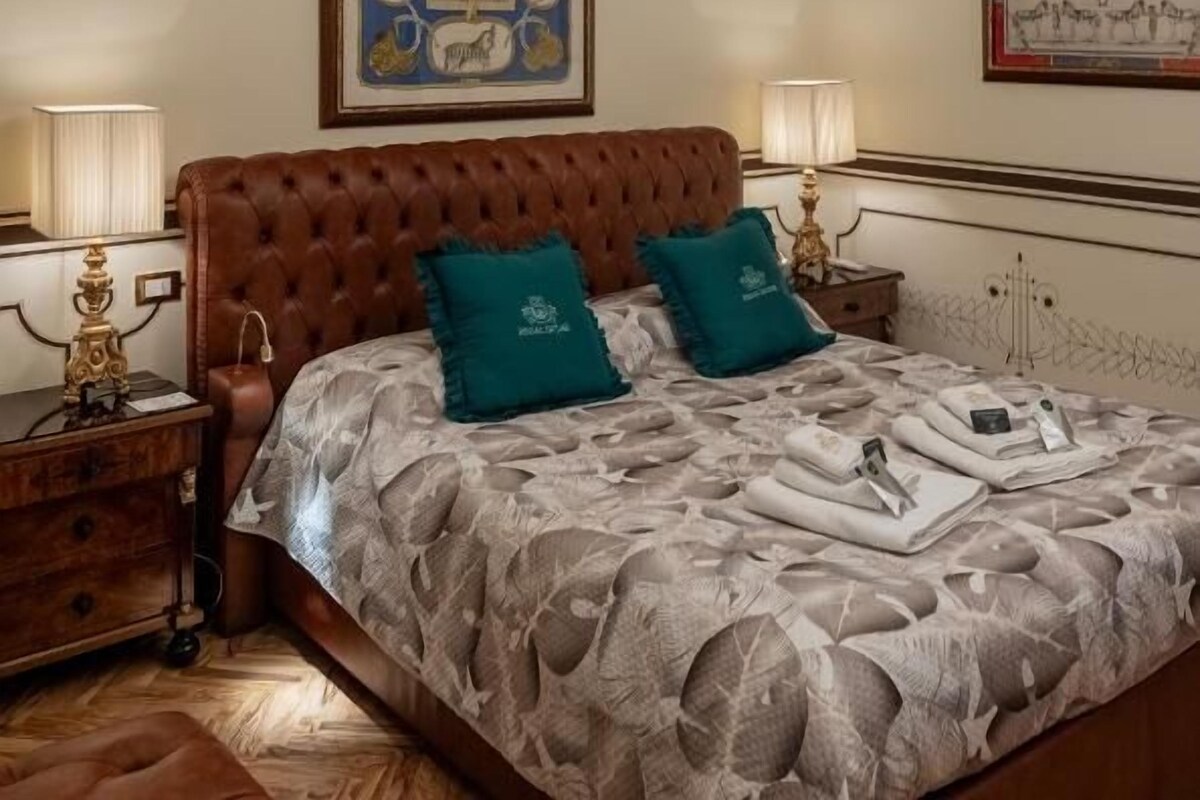 A bedroom with a tufted headboard, two bedside lamps, a framed artwork above the bed, and a chandelier.