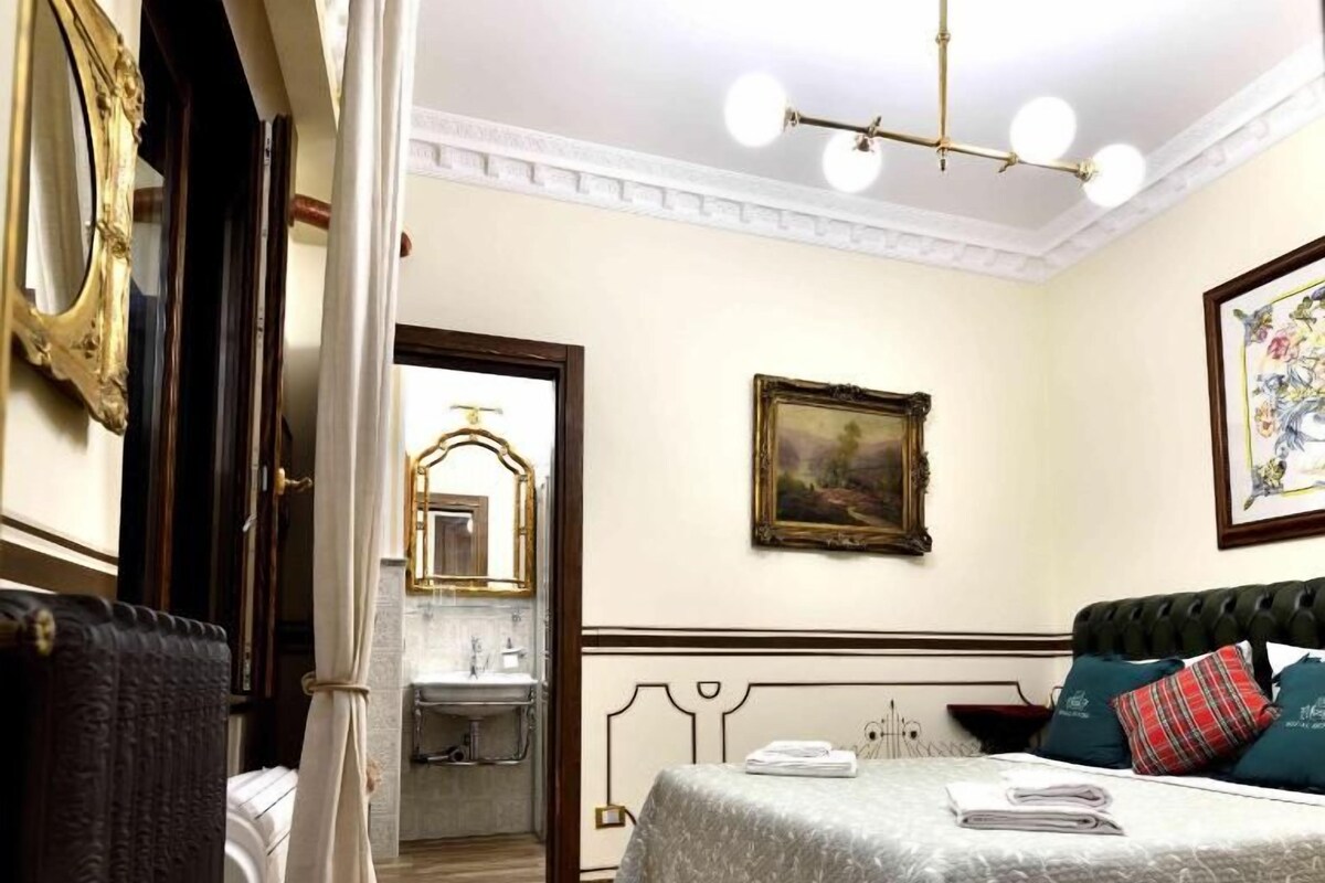 A hotel room with a bed, a nightstand, a mirror, a picture frame, and a chandelier.