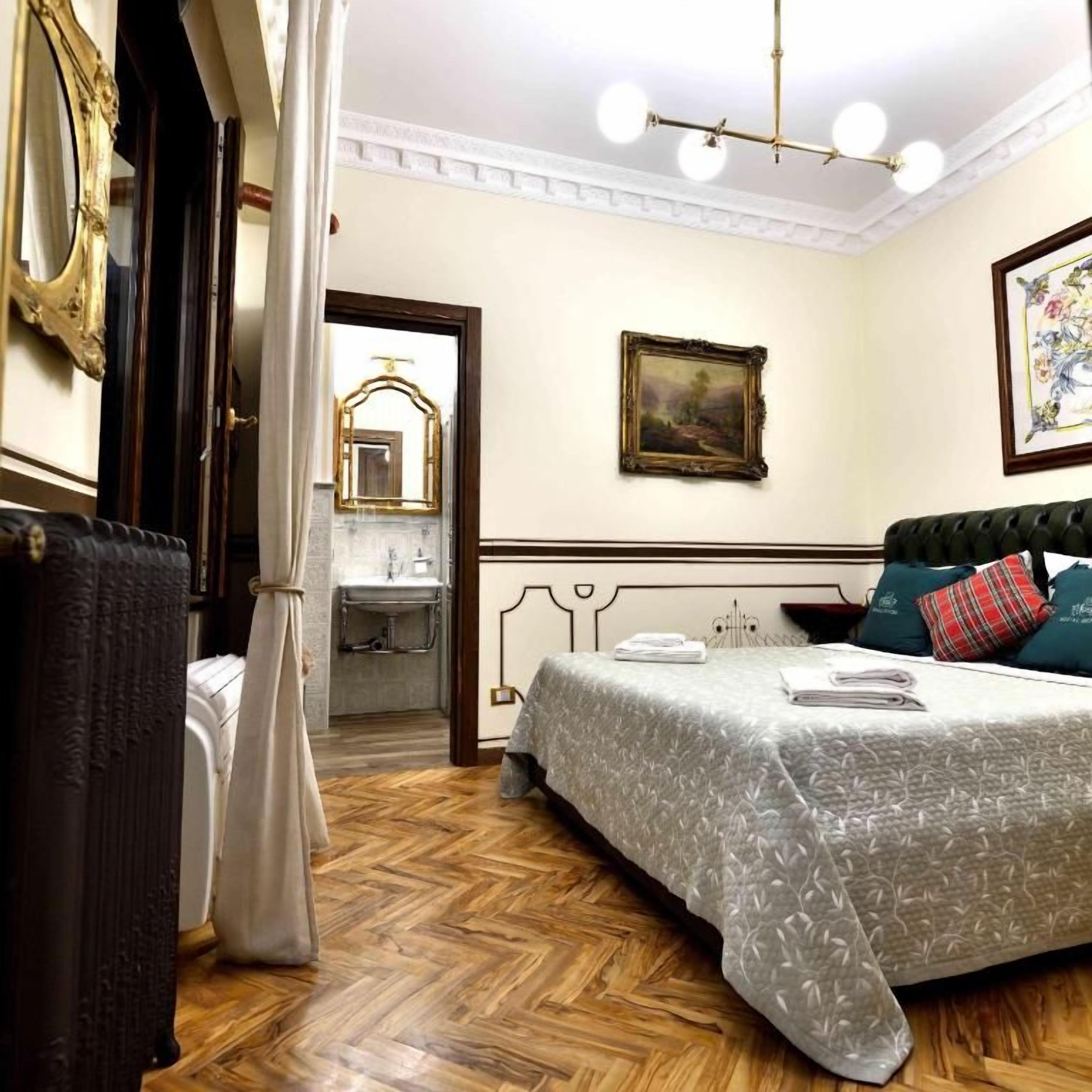 A hotel room with a bed, a nightstand, a mirror, a picture frame, and a chandelier.