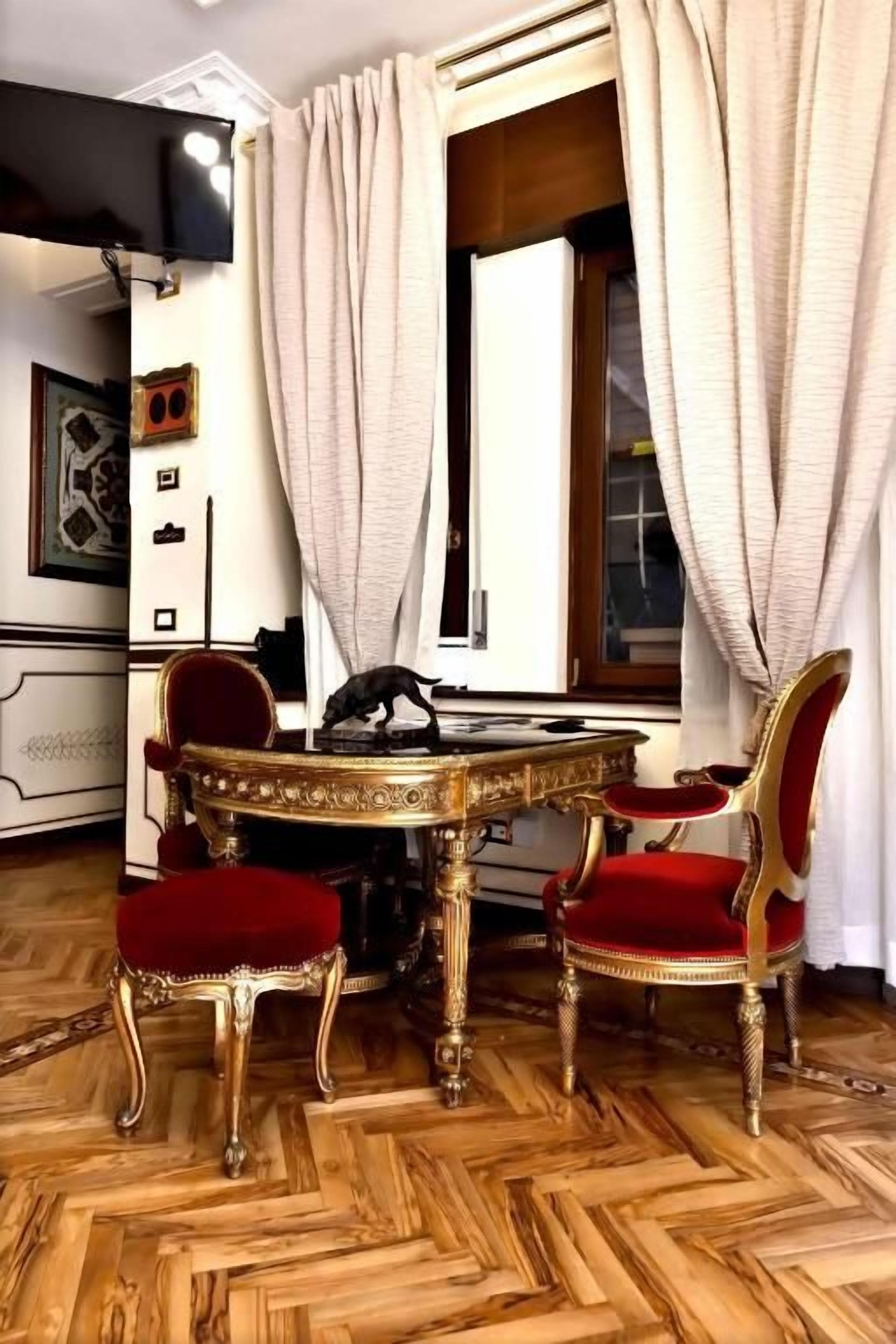 A room with a round table, two chairs, and a window with curtains.