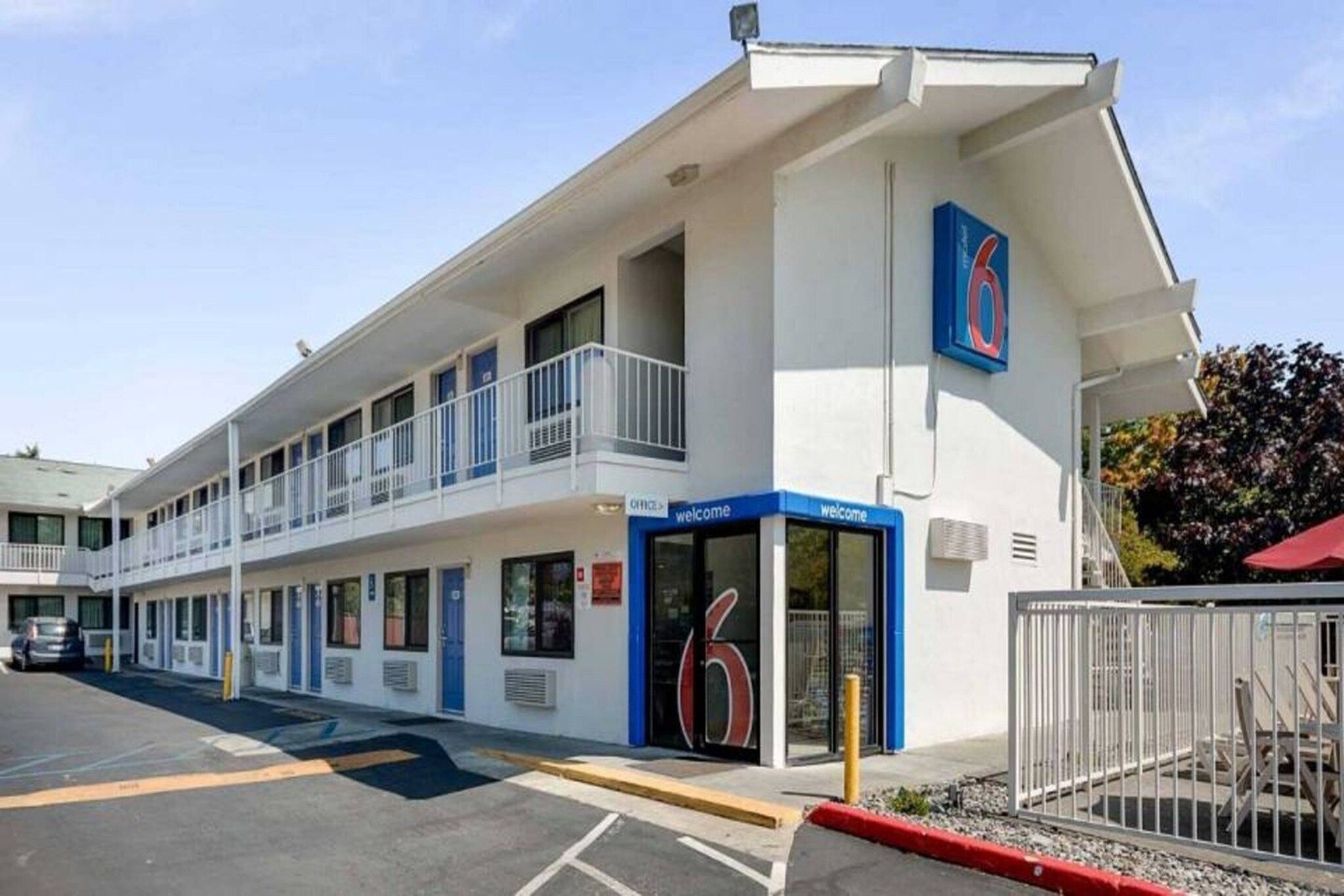 A motel with a blue entrance, a balcony on the second floor, and a parking lot.