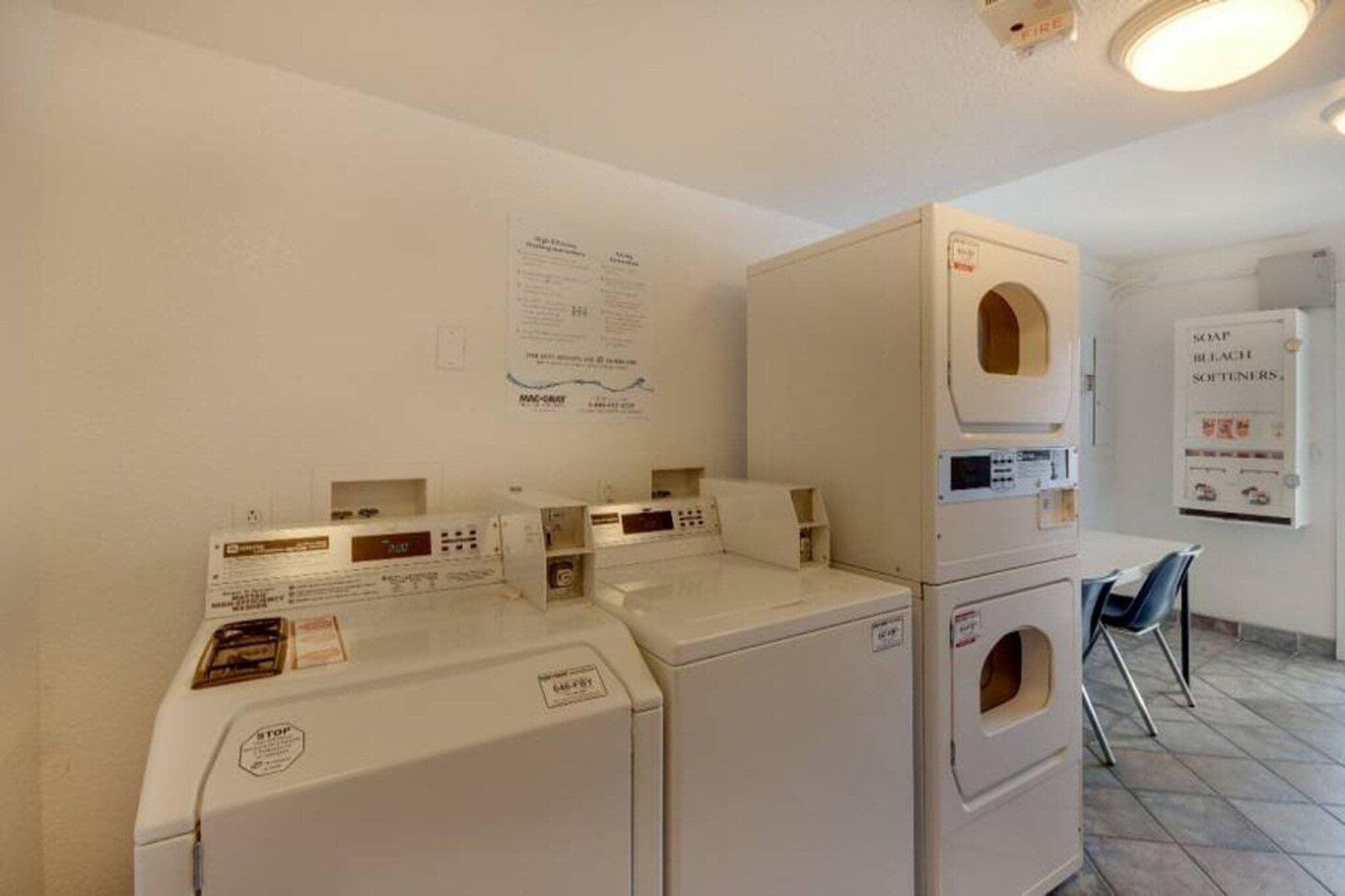 A laundry room with stacked washers and dryers, a fire alarm, and a notice board.