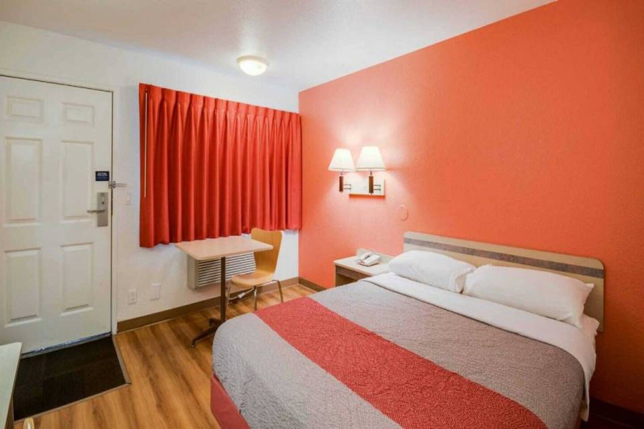 A hotel room with a bed, a desk, a chair, a nightstand, and a telephone.