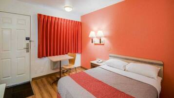 A hotel room with a bed, a desk, a chair, a nightstand, and a telephone.