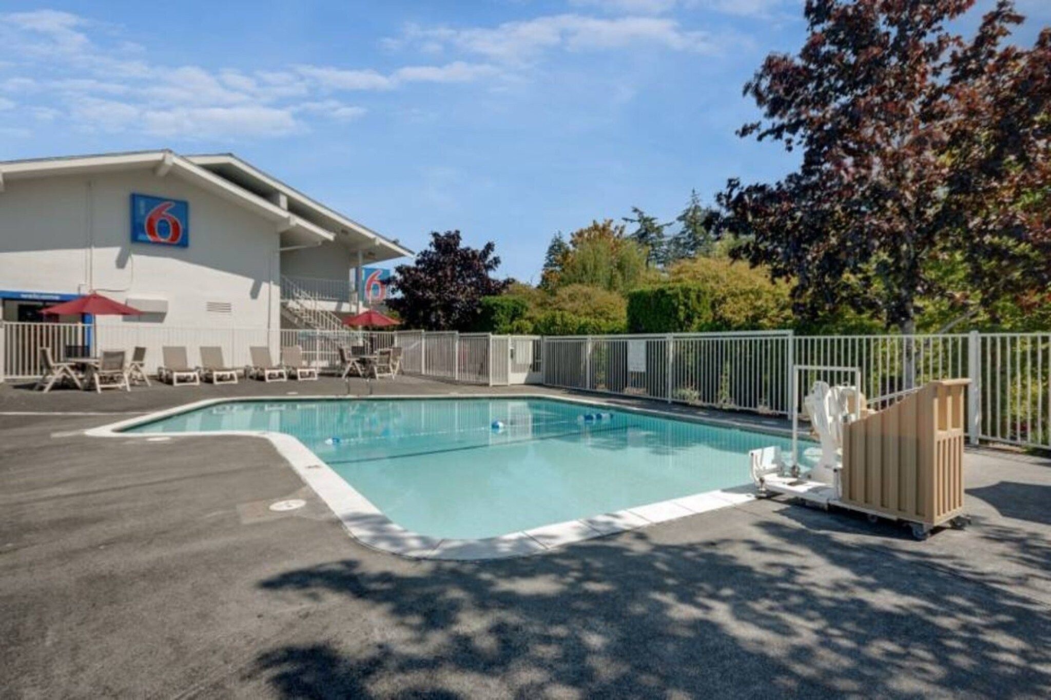 A swimming pool with a fenced deck, lounge chairs, and a building with a logo in the background.