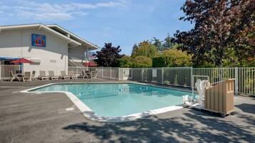 A swimming pool with a fenced deck, lounge chairs, and a building with a logo in the background.