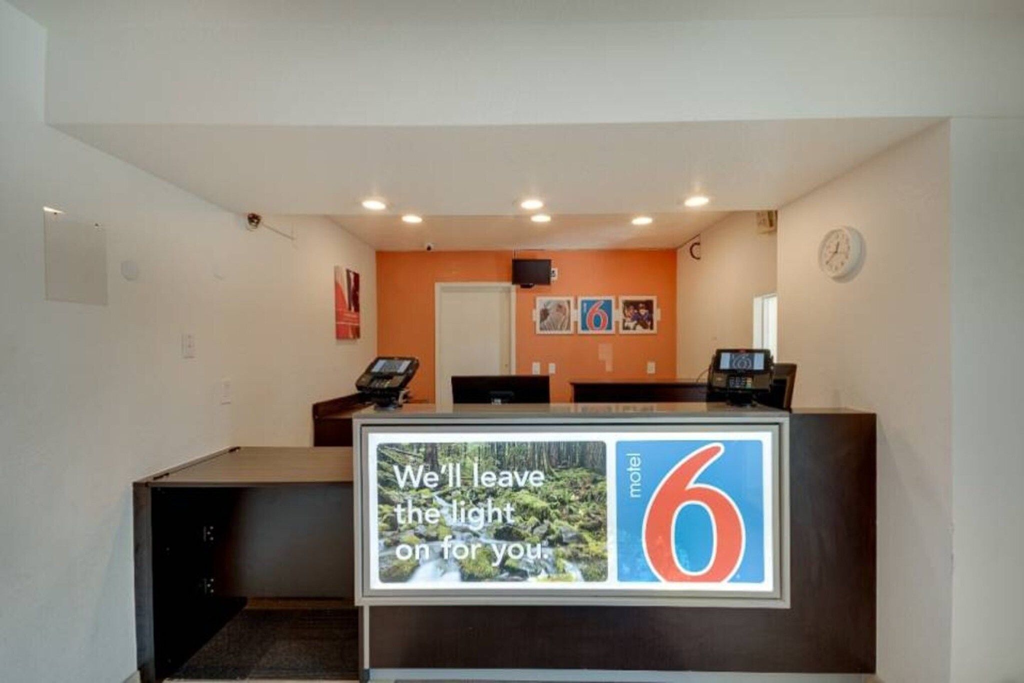 A motel reception desk with a large number '6' sign, a clock, and a digital display.