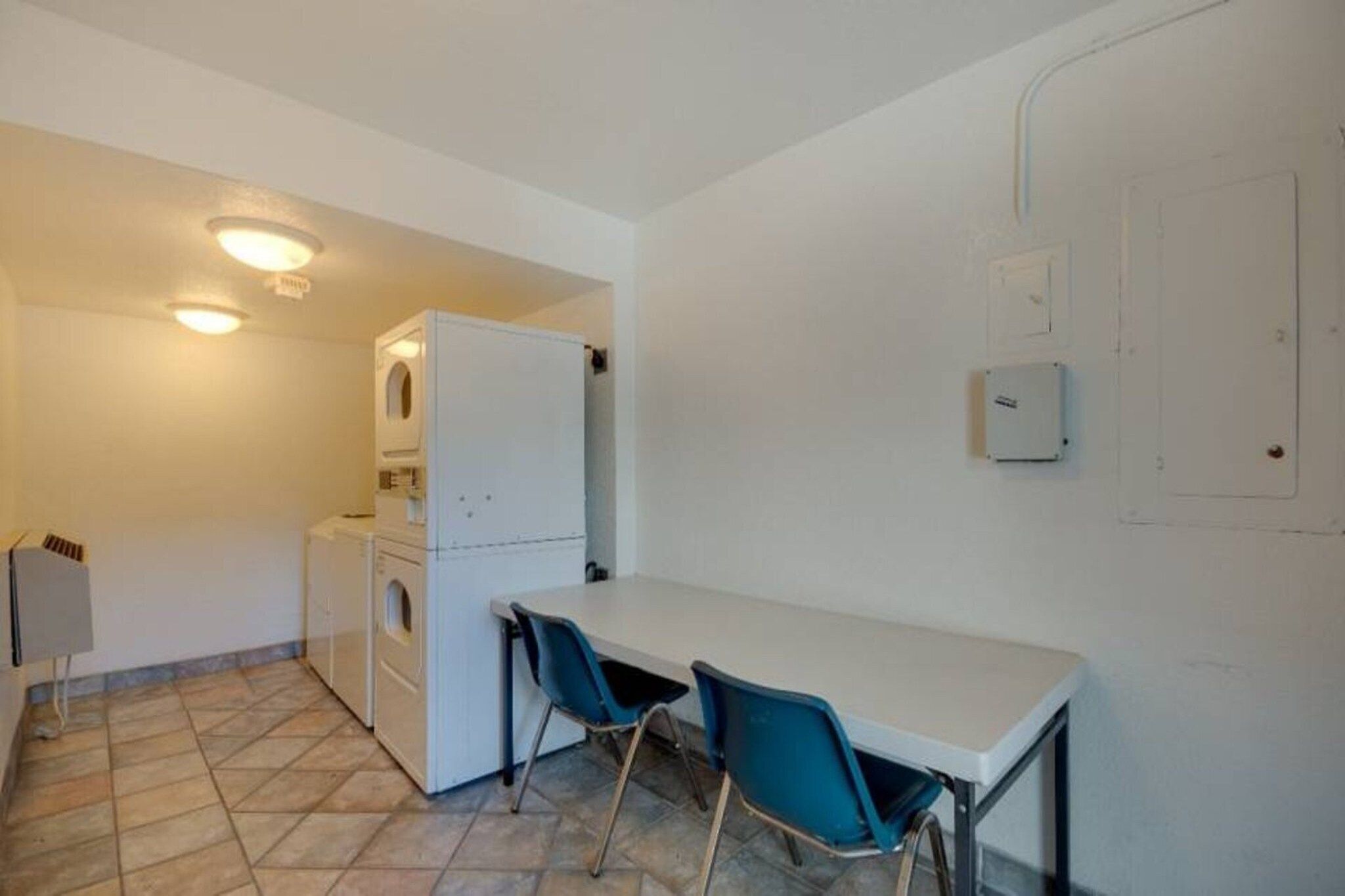 A compact kitchen with a white refrigerator, a washing machine, and a small table with two chairs.