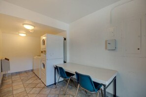 A compact kitchen with a white refrigerator, a washing machine, and a small table with two chairs.