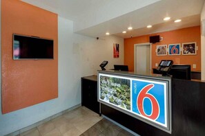 A reception desk with a digital display, a television mounted on the wall, and a door in the background.