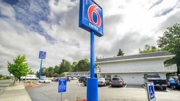 A motel with a blue sign indicating the entrance, a parking lot with several cars, and a building with a white facade.
