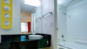 Un baño con encimera negra, lavabo blanco y ducha con mampara de vidrio.
