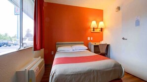 Habitación de hotel con cama, calefacción, escritorio con silla y ventana con vistas al exterior.