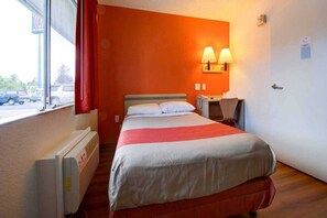 Une chambre d’hôtel équipée d’un lit, d’un radiateur, d’un bureau avec une chaise et d’une fenêtre donnant sur l’extérieur.