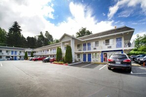 A motel with multiple-story buildings, a parking lot, and a clear sky. - 1 Queen Bed | Micfridge (Seattle)