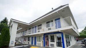 Un motel de dos pisos con una decoración azul y blanca, un número '6' en la entrada y una escalera visible que conduce al piso superior.