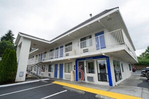 Un motel à deux étages, aux couleurs bleu et blanc, avec une entrée marquée du chiffre « 6 » et un escalier bien visible menant à l’étage supérieur.