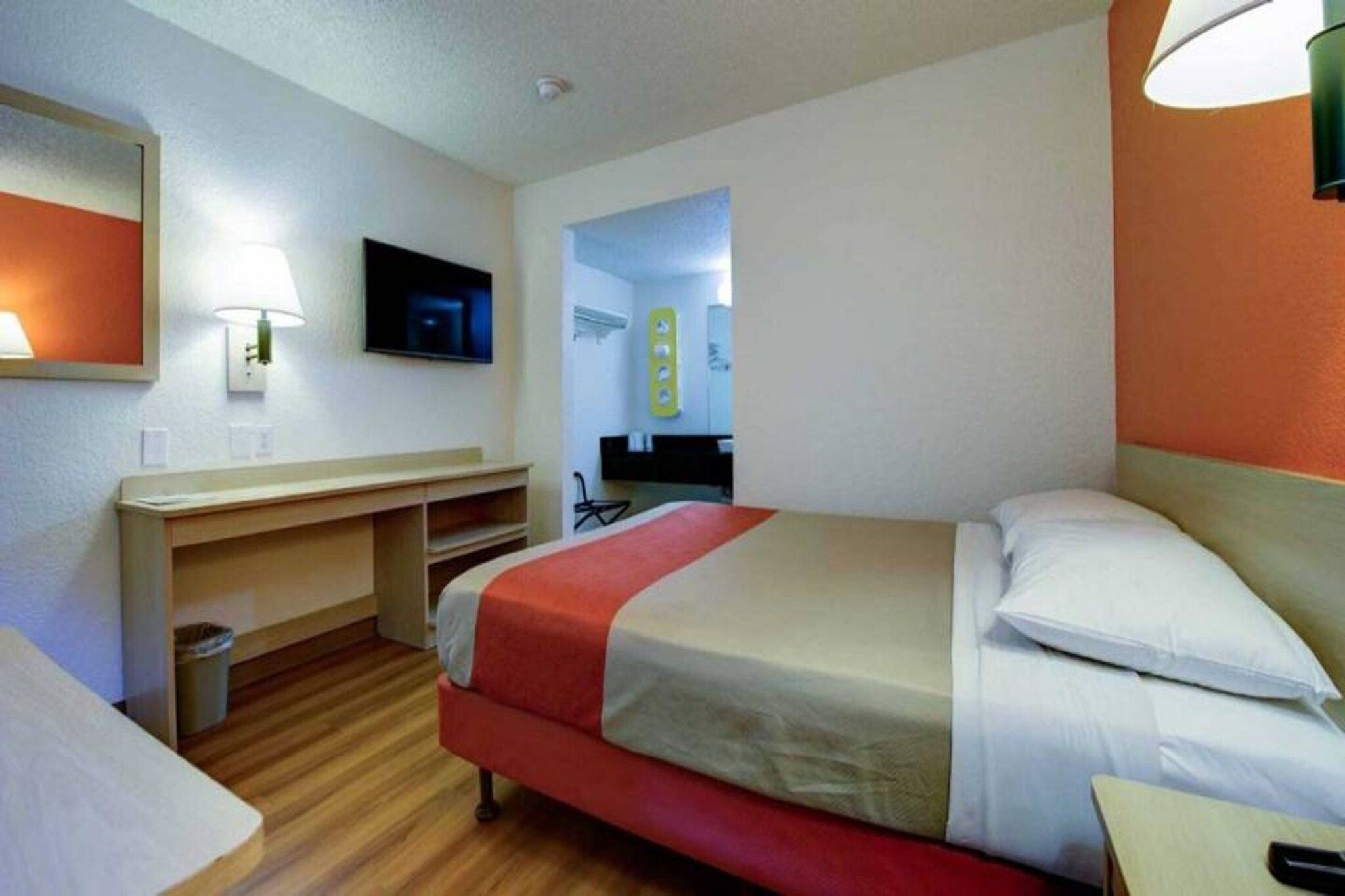 A hotel room with a bed, a desk, a chair, a television, and a bathroom visible through an open door.