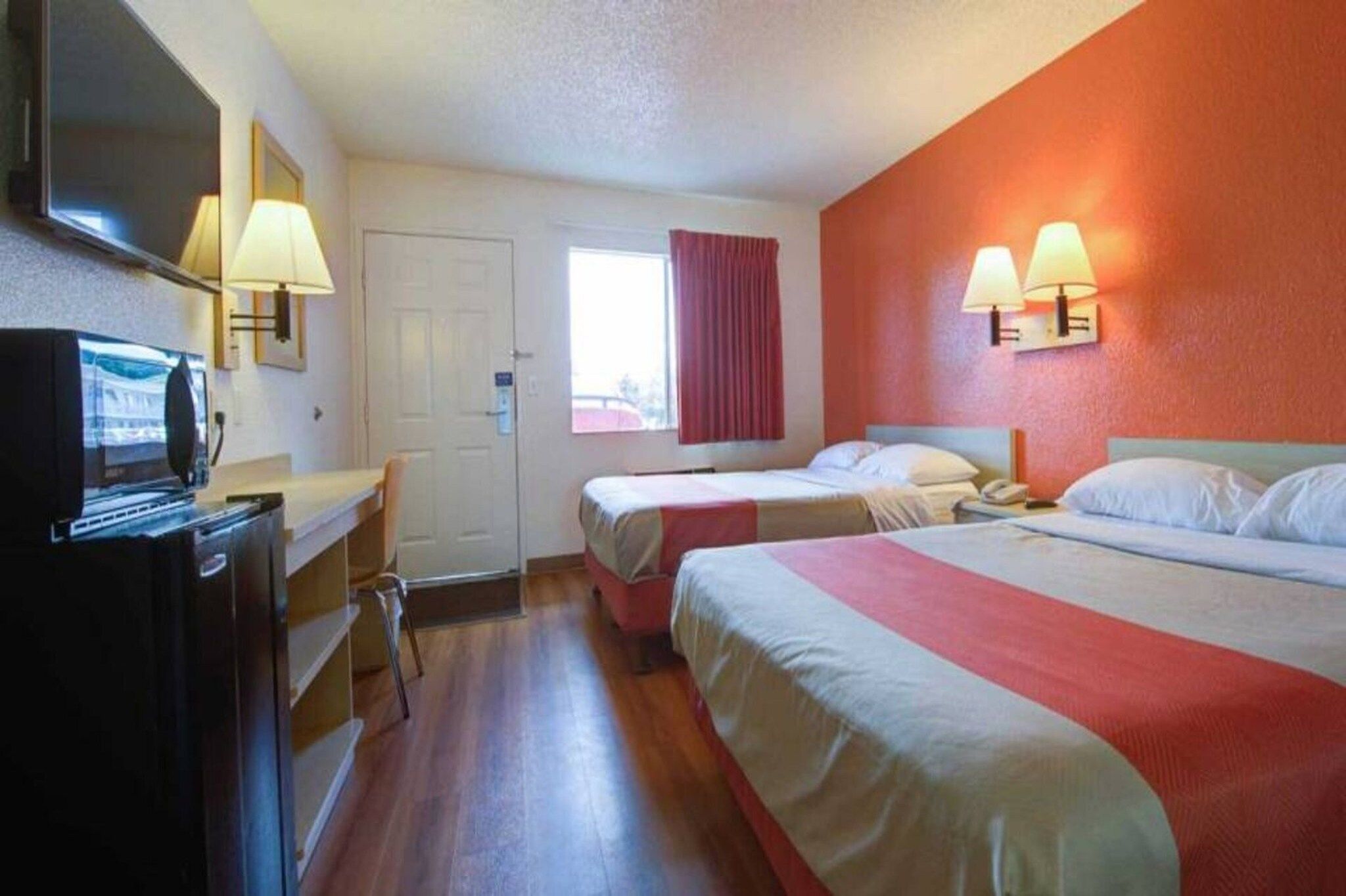 A hotel room with two beds, a desk, a TV, and a window with curtains.