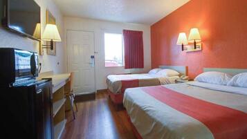 A hotel room with two beds, a desk, a TV, and a window with curtains.