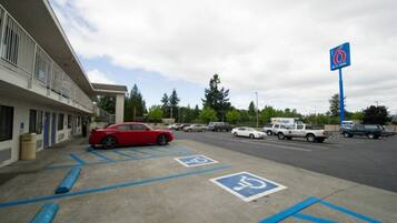 A parking area with marked handicapped spaces, a red car parked, and a building with a blue sign in the background.