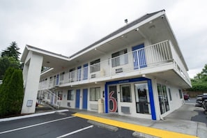 Um motel de dois andares com fachada azul e branca, um letreiro de 'Welcome' e um estacionamento.
