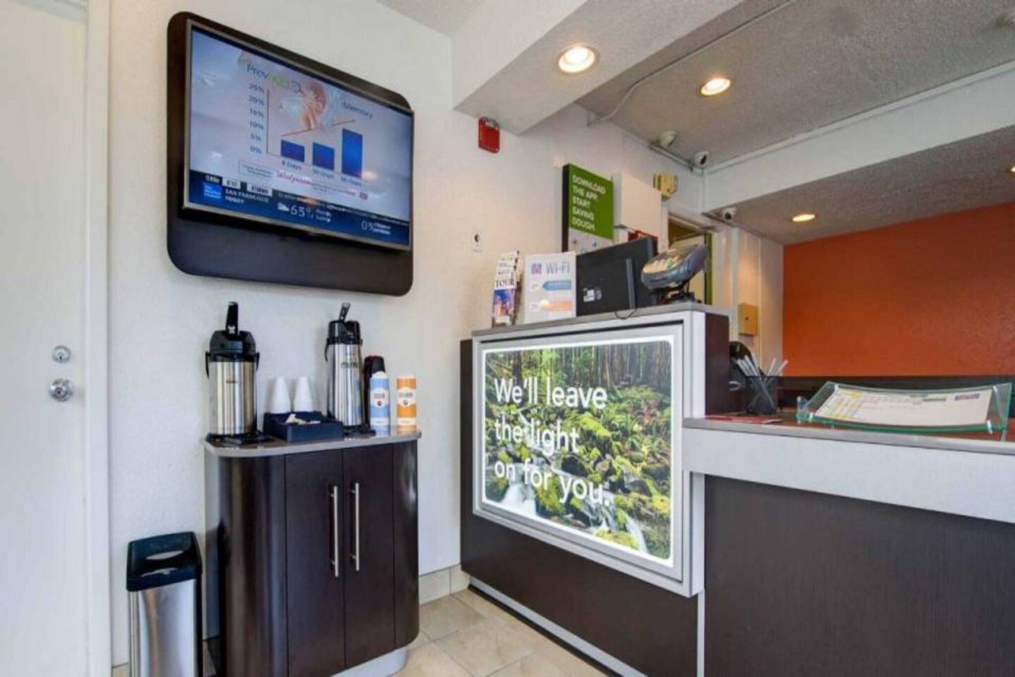 A reception area with a digital screen displaying a graph, a coffee station, and a sign with a message.