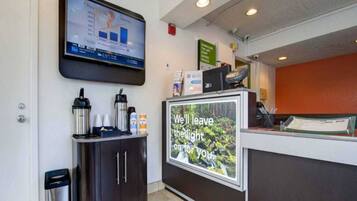 A reception area with a digital screen displaying a graph, a coffee station, and a sign with a message.