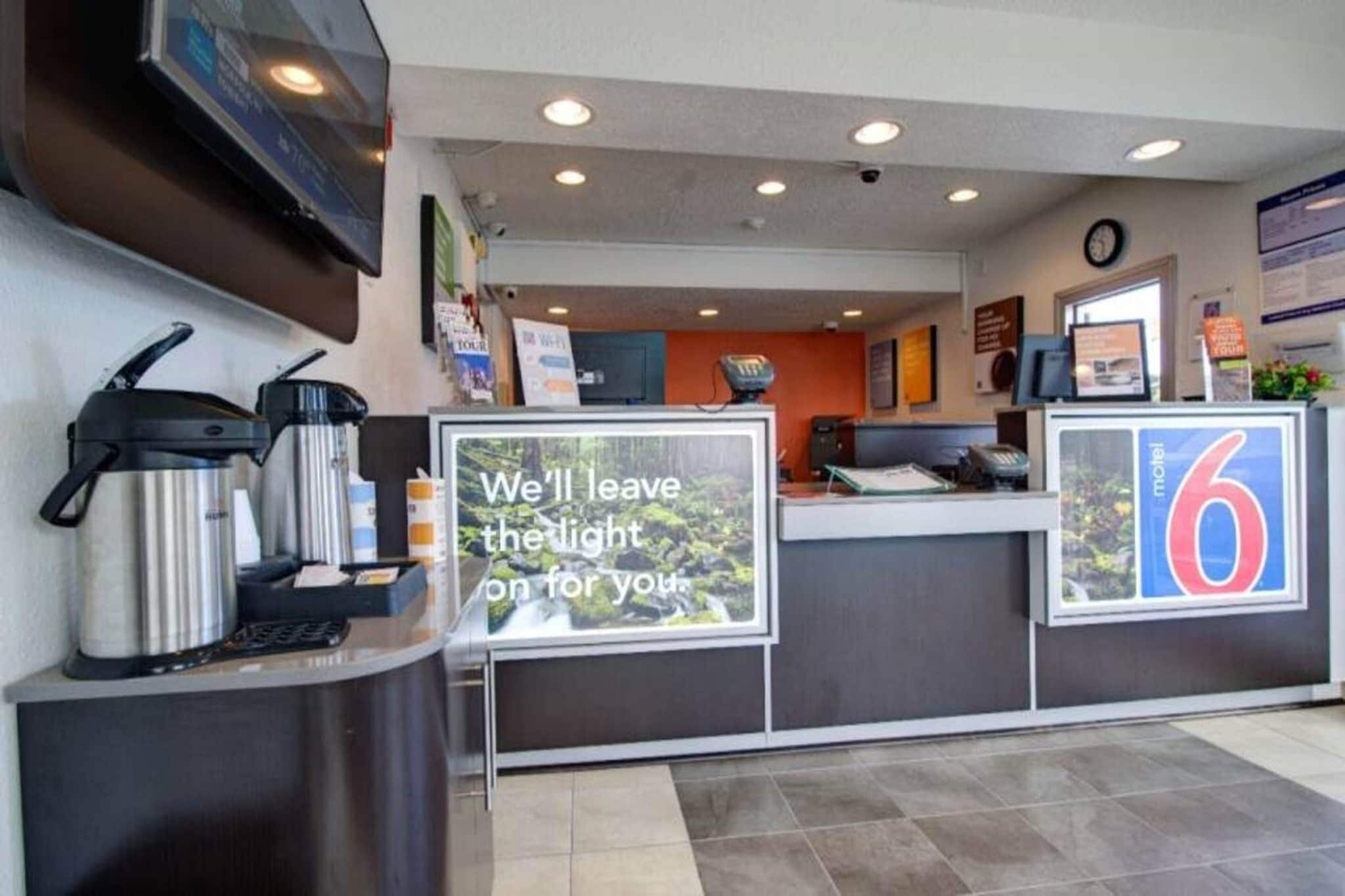 A hotel reception area with a coffee machine, a sign stating 'We'll leave the light on for you,' and a number '6' indicating the room number.