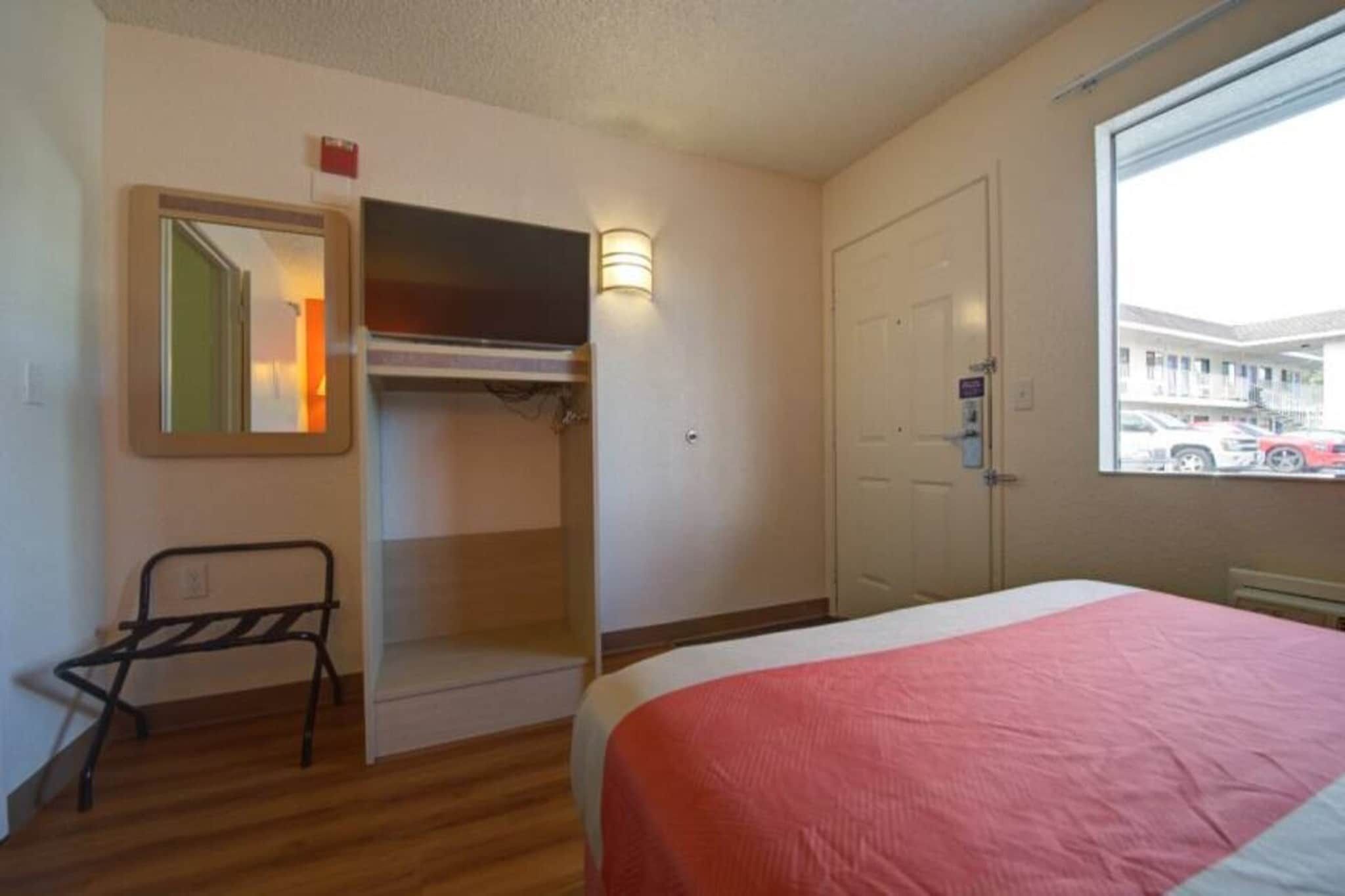 A hotel room with a bed, a wardrobe, a mirror, and a window with a view of the outside.
