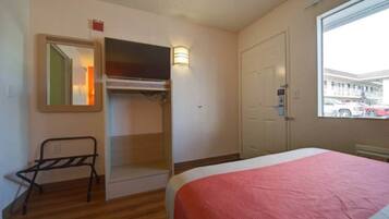 A hotel room with a bed, a wardrobe, a mirror, and a window with a view of the outside.