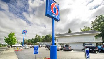 A motel with a prominent '6 ENTER' sign, a parking lot with several cars, and a building in the background.