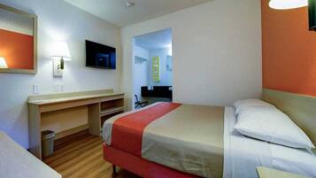 A hotel room with a bed, a desk, a chair, a television, and a bathroom visible through an open door.