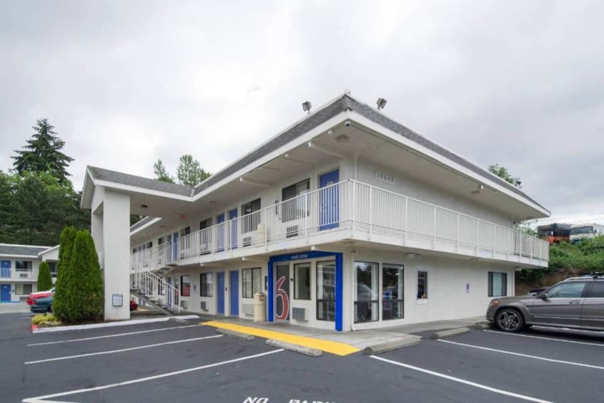 A multi-story motel with a flat roof, a central entrance, and a parking lot.